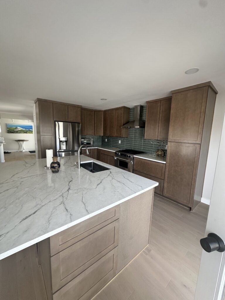 Finished kitchen remodel with stained shaker cabinets, white quartz island and green glass subway tile backsplash