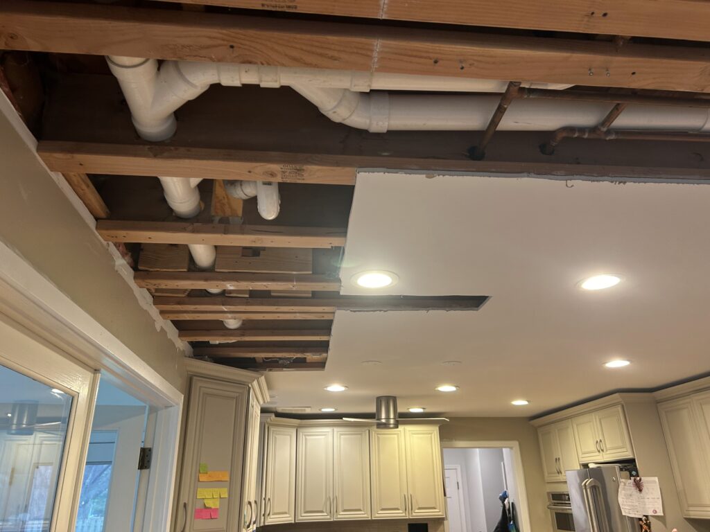 Kitchen ceiling opened to expose joists and plumbing before drywall repair