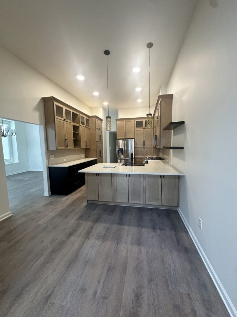 Finished kitchen with glass-front upper cabinets, quartz peninsula and cylinder pendant lights