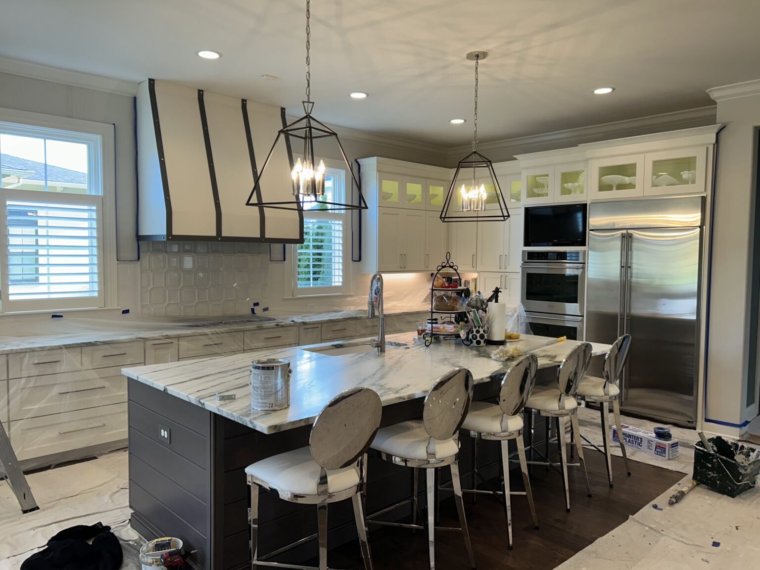 Large white kitchen with a cream range hood, marble island and pendant lights during a Mister Painter Group remodel
