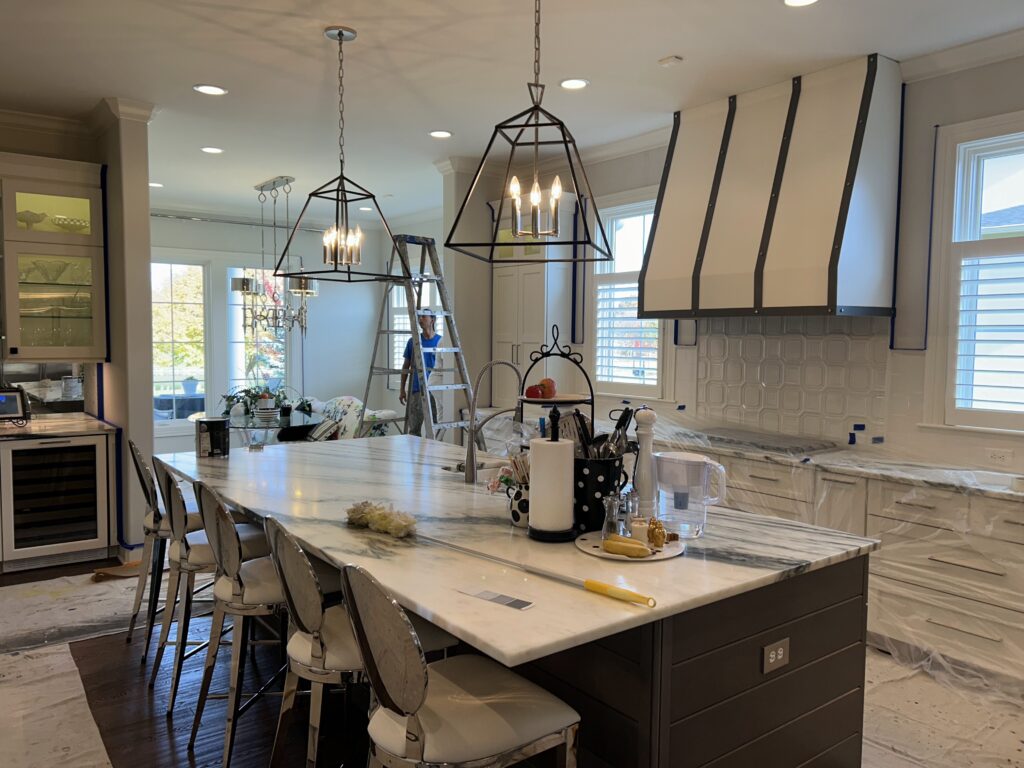 White painted kitchen cabinets with a dark shiplap island, marble top and geometric pendant lights